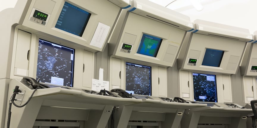 A row of three large air traffic control systems with maps displayed on their screens.