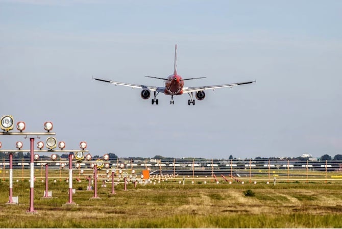 A red aircraft coming in for landing just above the runway. Approach lights can seen in the foreground.