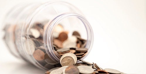 A jar filled with coins, tipped on its side, with the coins spilling out.