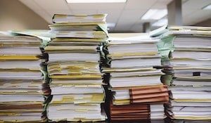 Four tall stacks of very thick books and document folders sitting on a desk.