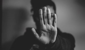 A person holding their palm up to the camera, in front of their face, communicating a 'stop' instruction.