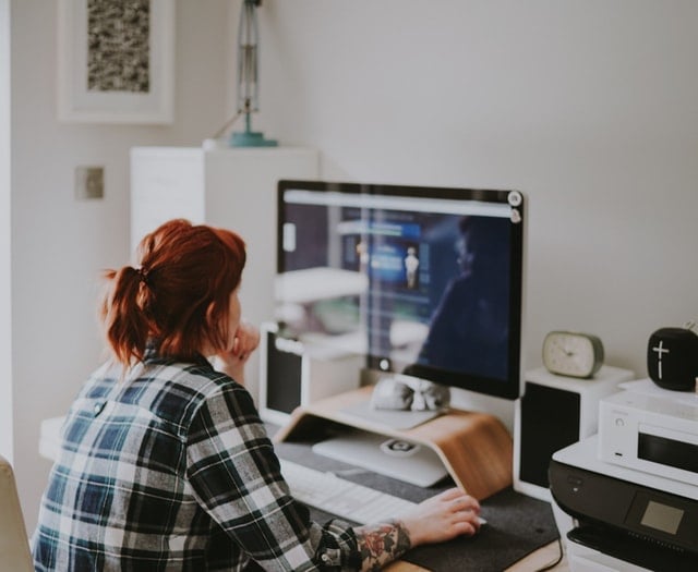 A person sat in front of a large computer monitor in a home office.