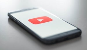 A smartphone on a table with the red YouTube logo displayed against a white background.