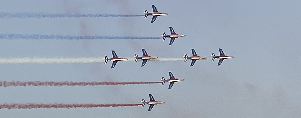 The Patrouille de France, a precision aerobatics unit in the French Air and Space force, flying in formation. They are leaving blue, white and red smoke trails behind them.