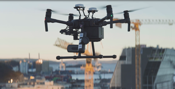 A black drone hovering at high altitude above an urban location where construction is happening.